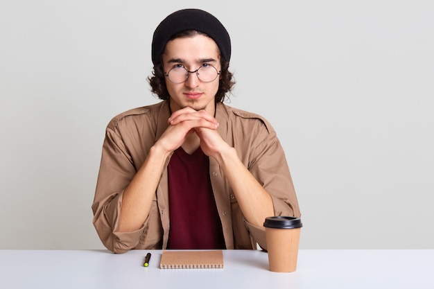 Indoor shot of young man keeps hands under chin