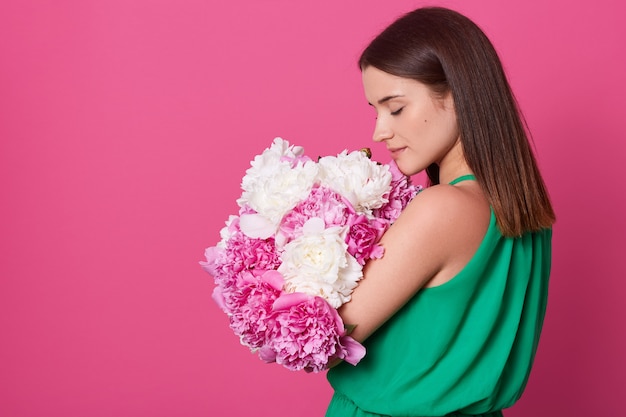 Indoor studio shot of sweet adorable young woman standing isolated over pink