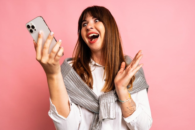 Indoor studio winter portret van brunette vrouw dragen joggers en trui met haar smartphone, opgewonden emoties.