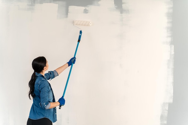 Vista interna della donna bruna che guarda il muro mentre dipinge con una speciale attrezzatura per la riparazione del rullo nella sua stanza e si sente soddisfatta