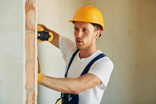 Indoors in unfinished room Young man working in uniform at construction at daytime