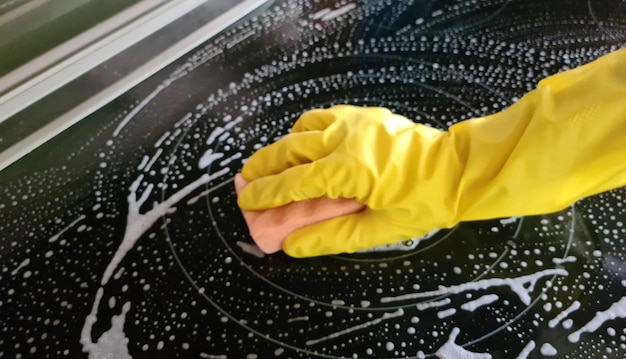 Inductiekookplaat schoonmaken Vrouw in gele rubberen handschoenen maakt de inductiekookplaat van de keuken schoon met reinigingsspray en spons