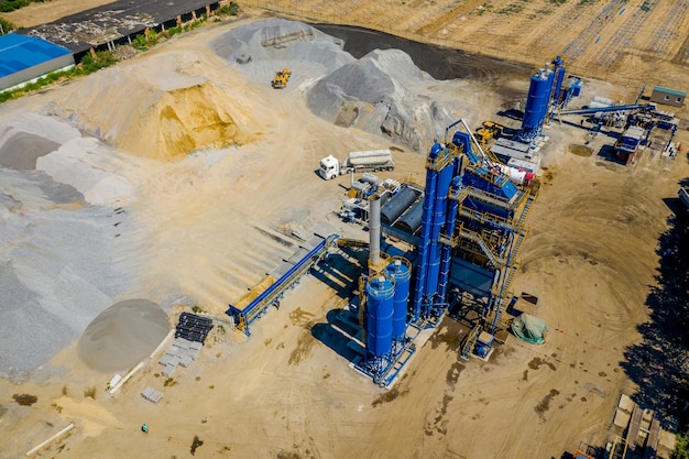 An industrial asphalt plant surrounded by piles of gravel.