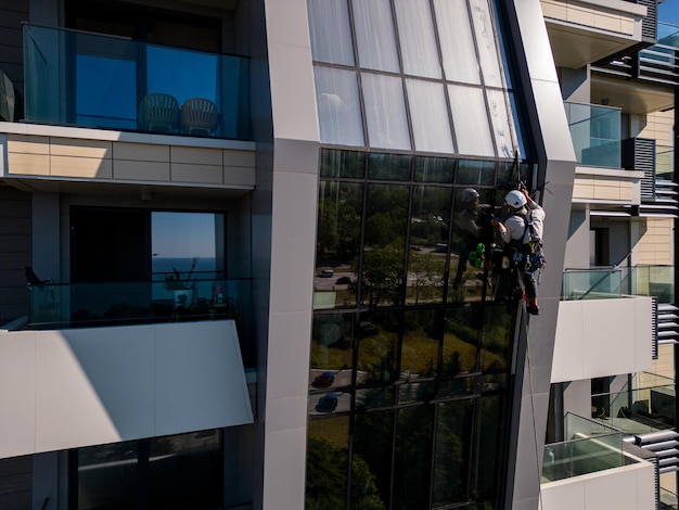 Industrial climber performs tasks at a great height on a glass wall of a tall building Drone video