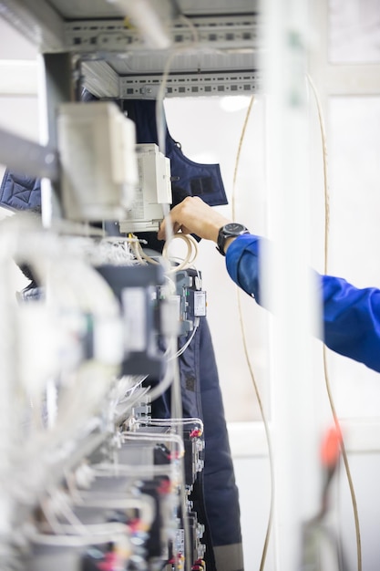 Industrial concept. A man standing by the control panels. White wires. Vertical shot