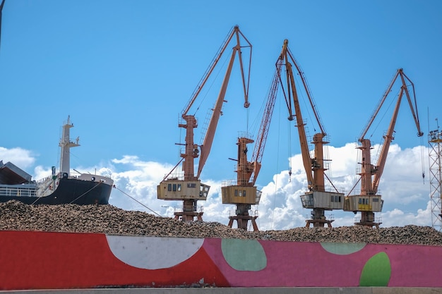 Industrial cranes in the port against blue sky and a fence with colored drawings in the foregroud