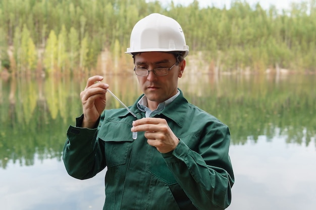 Industrial ecologist or chemist takes a sample of water from lake at the site of a flooded quarry