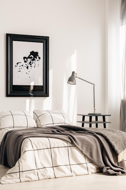 Industrial lamp on nightstand table next to king size bed in white bedroom interior