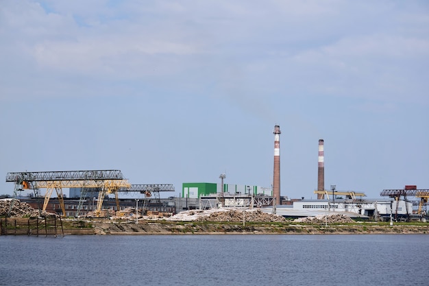 Industrial landscape, pulp and paper mill with stacks of logs and chimneys by the river