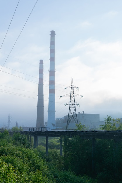 Индустриальный пейзаж, железнодорожные пути, уходящие в утренний туман, трубопроводы и дымоходы в тумане