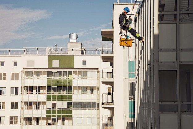 Промышленный альпинист висит над жилым домом во время мытья фасадного остекления. Рабочий висит на стене дома. Концепция городских работ. Копировать пространство