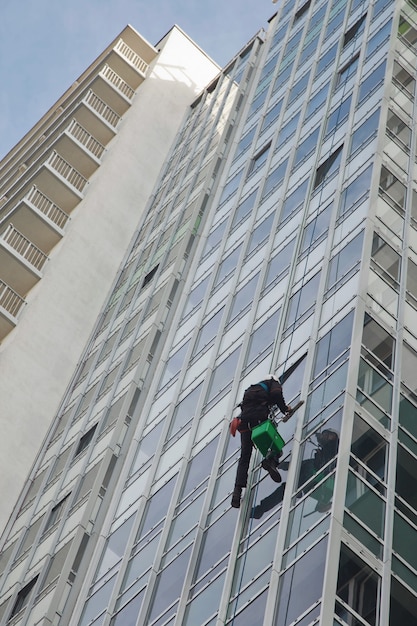 Industrial mountaineering worker hangs over residential building while washing exterior facade glazing. Rope access laborer hangs on wall of house. Concept of urban works. Copy space