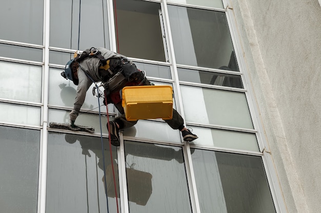 Industrial mountaineering worker hangs over residential facade\
building while washing exterior facade glazing. rope access laborer\
hangs on wall of house. concept of industry urban works. copy\
space