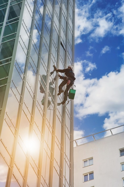 Промышленный альпинист, моющий наружное фасадное остекление, висит над жилым фасадом здания