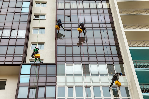 Industrial mountaineering workers hangs over residential facade building while washing exterior facade glazing. Rope access laborers hangs on wall of house. Concept of industry urban works. Copy space