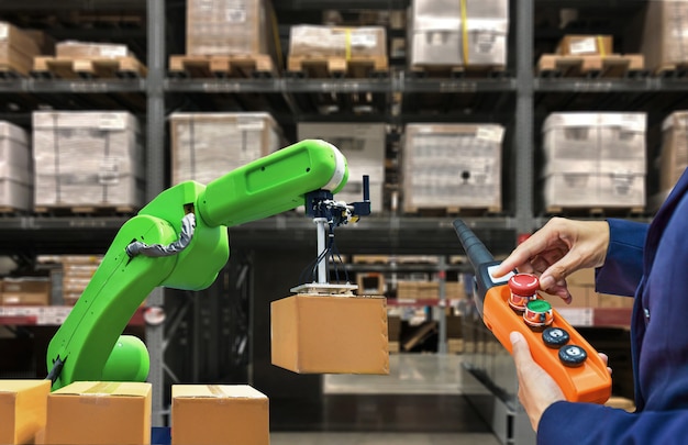 Photo industrial robot holding a box and worker operating a robot machine with a control panel on stock shelves