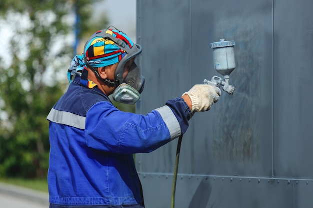 Industrial work Priming of metal products from the compressor gun A worker in overalls and a protective mask paints the body of a truck trailer or a metal car