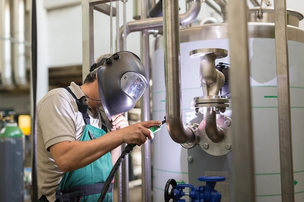 Operaio industriale con maschera protettiva saldatura elementi inox in strutture in acciaio fabbricano officina o fabbrica di metallo.