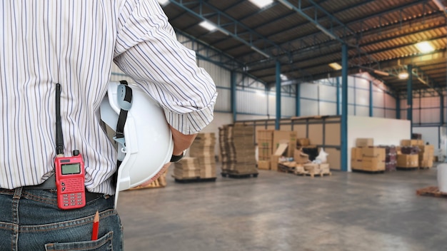 Industrieel ingenieur man staande en zet walkie talkie in jeans pakket met veiligheidshelm. werknemersvrouw die de constructie controleert met een wazige grote magazijnachtergrond concept engineer werkt op locatie.