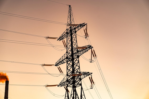 Industrieel landschap: toren van hoogspanningslijnen op een achtergrond van oranje lucht. Zendvermogen, power tower op een lege landbouwgrond bij de zonsondergang