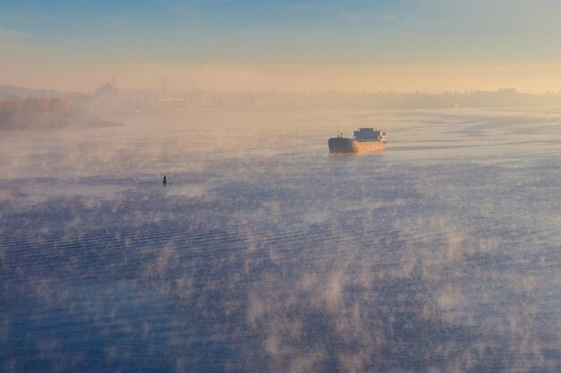 Industrieel schip dat 's ochtends in de mist over de rivier vaart