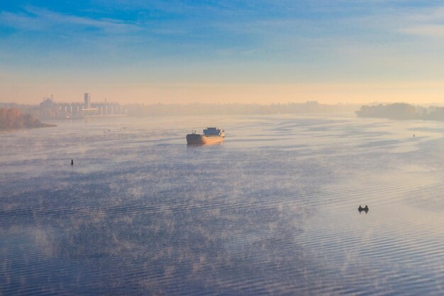 Industrieel schip dat 's ochtends in de mist over de rivier vaart