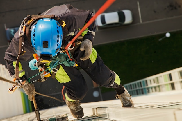 Industriële bergbeklimmer hangt over woongebouw tijdens het wassen van buitengevelbeglazing. Rope access arbeider hangt aan de muur van het huis. Concept van stedelijke werken. Ruimte kopiëren