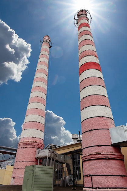 Industriële fabrieksschoorstenen. Stadsverwarmingsinstallatie buitenkant met industriële schoorstenen tegen de zon en de blauwe lucht. Lage kijkhoek.