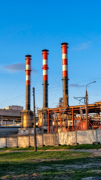 Industriële ondernemingen met pijpen tegen de blauwe lucht.