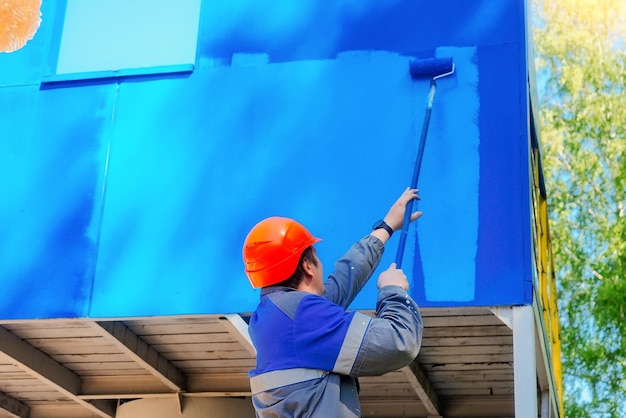 Industriële professionele schilder in helm en werkkleding schildert metalen oppervlak met roller