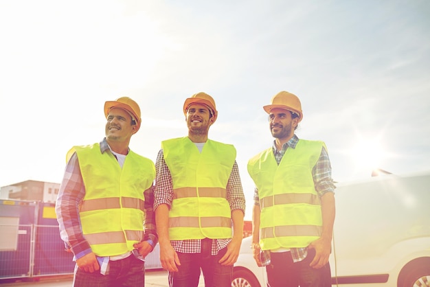 industry, building, construction and people concept - happy male builders in high visible vests outdoors