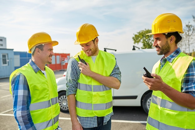 industry, building, technology and people concept - happy male builders in high visible vests with walkie talkie or radio outdoors