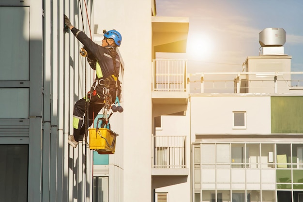 Lavori urbani del settore il lavoratore di alpinismo industriale in uniforme si blocca su un edificio residenziale sullo sfondo della città