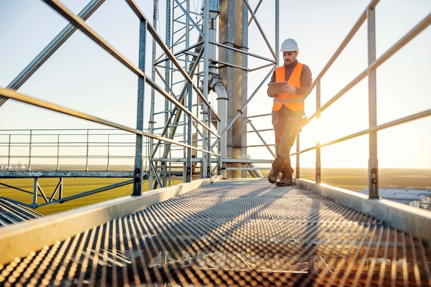 An industry worker scrolling on tablet while standing on height