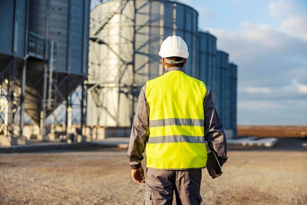 An industry worker walking towards silos with tablet in his hands