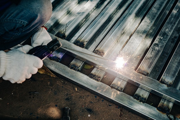 写真 白い手袋をかぶった産業労働者作業中の溶接鉄屋外で鋼を溶接するためのクローザップハンドツール建設用溶接機を使用する産業概念
