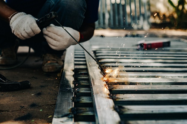 Foto lavoratore dell'industria che indossa guanti bianchi e ferro da saldatura al lavoro all'aperto strumento manuale di primo piano per la saldatura dell'acciaio concetto industriale che utilizza una macchina da saldatura per la costruzione