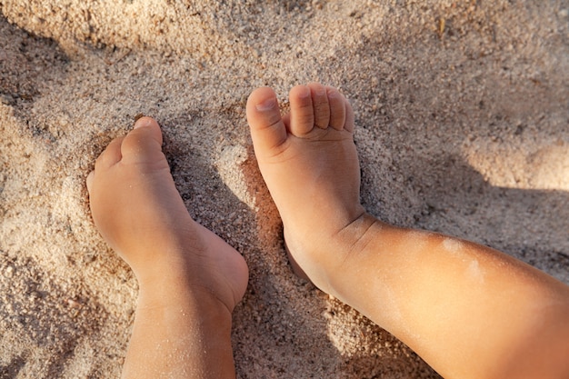 Photo infant baby feet on sandy beach as a background, childhood and vacation concept