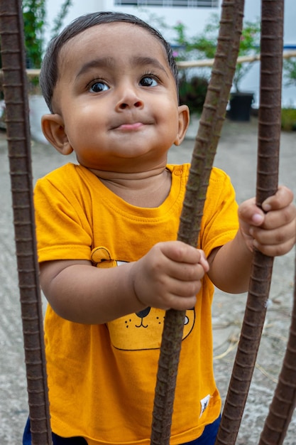 A infant child is trying to stand up holding a rusty iron rod in his small two hands A kid is having fun and sticking out his tongue