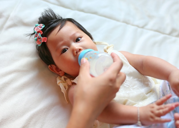 Infant girl feeding milk from bottle by mother hand.