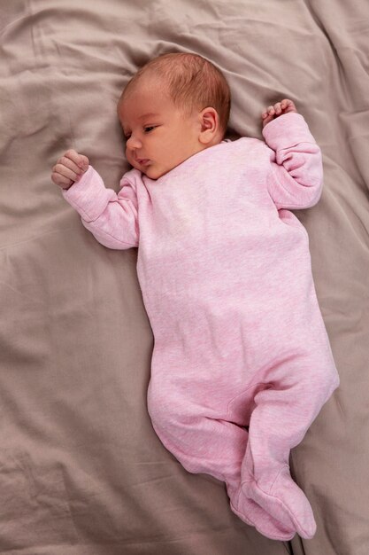 Photo an infant girl in pink clothes lies on the bed. love and tenderness. vertical.