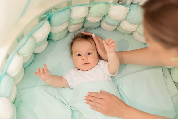 Infant lies on his back in a white round bed in the bedroom.