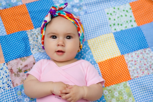 An infant lies on a patchwork quilt with a surprised look.