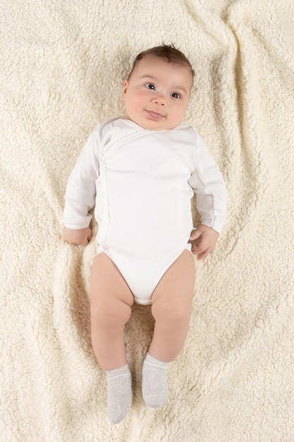 Un bambino in un body bianco giace su una morbida coperta mockup per cartoline pubblicitarie per la celebrazione del design