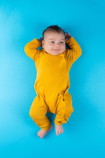 Un bambino in un body giallo giace su uno sfondo blu divertente piccolo bambino mockup per cartoline pubblicitarie per la celebrazione del design