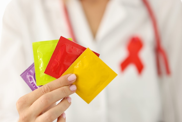 Infectious disease doctor with red ribbon on uniform holds lot of condoms in hand closeup