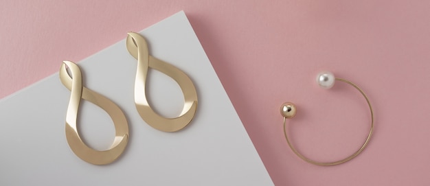 Infinity symbol shape earrings and modern bracelet on pink and white paper