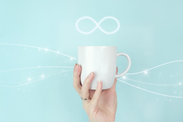 The infinity way to nowhere, business confusion concept. Cropped view of female hand with white coffee cup and sign infinity symbol on blue background.