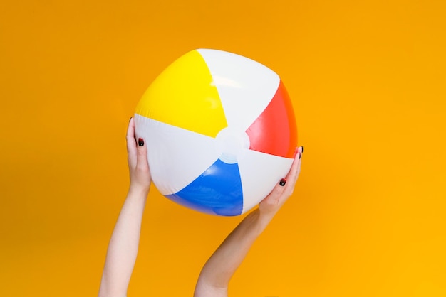 Inflatable ball for playing in the water and on the beach in\
hands on a yellow background vacation