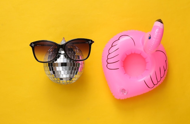 Inflatable flamingo with disco ball in sunglasses on yellow background Minimalism party concept